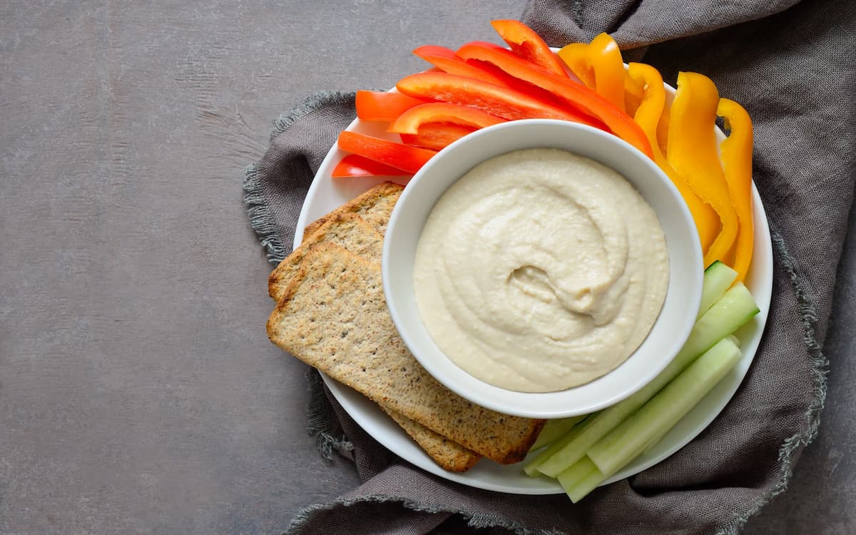 Bir kasede humus ve tabağın kenarlarında taze sebzeler var